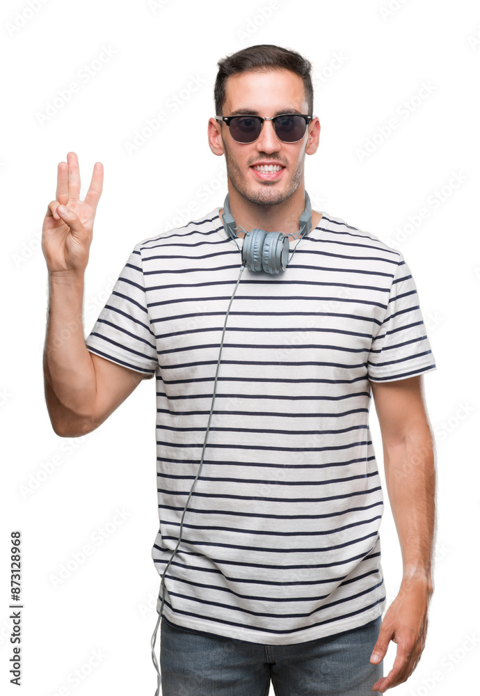 Handsome young man wearing headphones showing and pointing up with fingers number three while smiling confident and happy. Handsome young man wearing headphones showing and pointing up with fingers number three while smiling confident and happy.