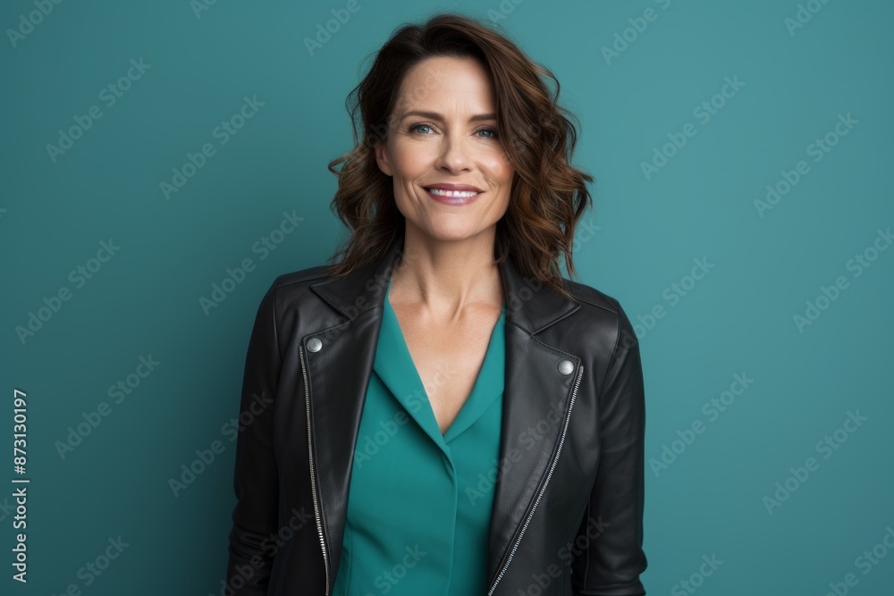 Portrait of a glad woman in her 40s sporting a stylish leather blazer in front of pastel teal background Portrait of a glad woman in her 40s sporting a stylish leather blazer in front of pastel teal background