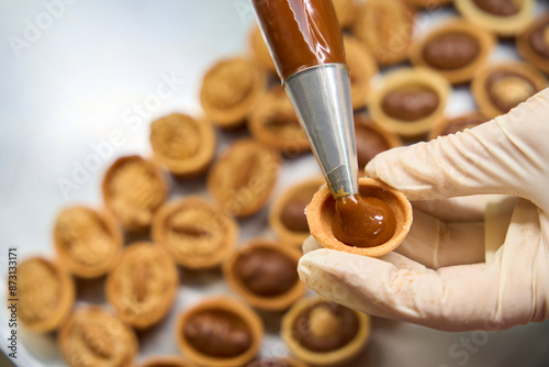 Close-up pastry-cook filling the nut cookies with chocolate fudge
