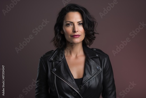 Portrait of a content woman in her 40s sporting a classic leather jacket isolated in pastel gray background © Markus Schröder
