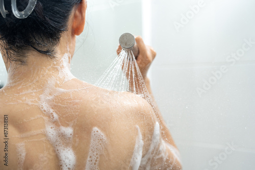 Female in shower rinse shampoo with water dripping on body. Young woman taking shower and washes soap bubbles off her body with water from the shower. Enjoying routine procedure at home.