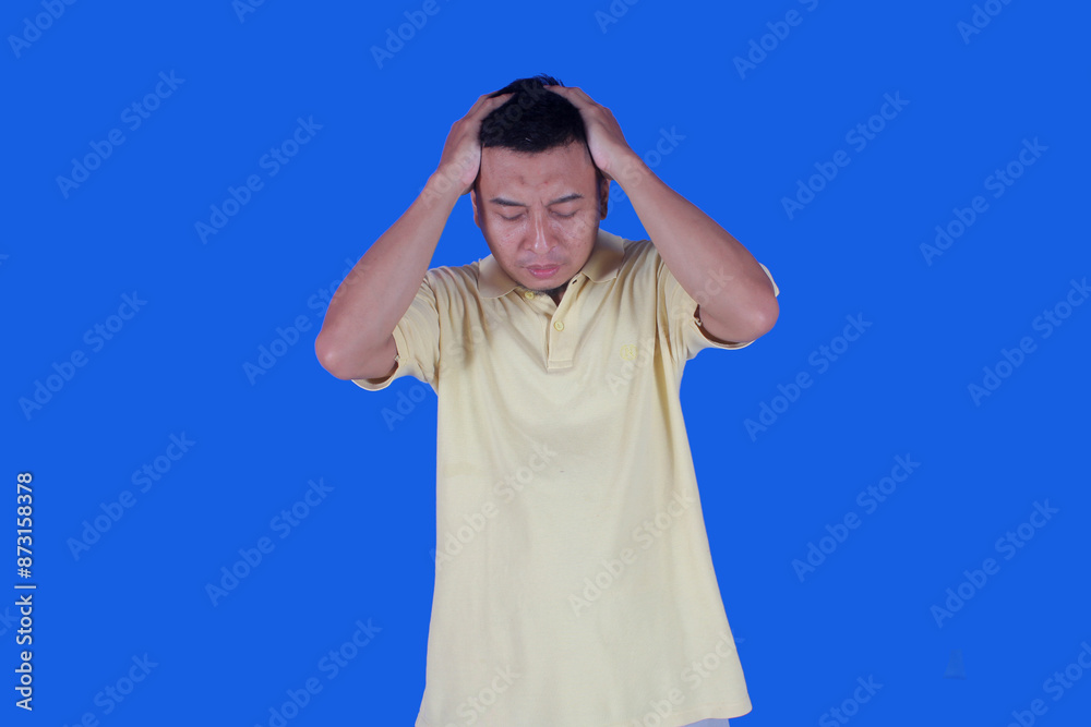 Portrait of handsome asian man dizzy while holding head with both hands isolated on blue background Portrait of handsome asian man dizzy while holding head with both hands isolated on blue background