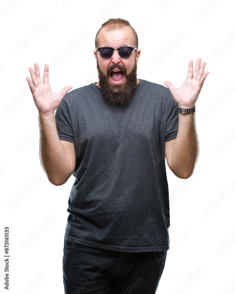 Naklejka premium Young caucasian hipster man wearing sunglasses over isolated background celebrating mad and crazy for success with arms raised and closed eyes screaming excited. Winner concept