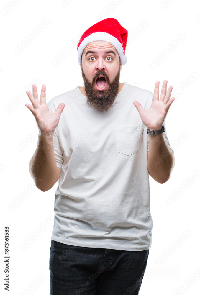 Young caucasian hipster man wearing christmas hat over isolated background celebrating crazy and amazed for success with arms raised and open eyes screaming excited. Winner concept Young caucasian hipster man wearing christmas hat over isolated background celebrating crazy and amazed for success with arms raised and open eyes screaming excited. Winner concept