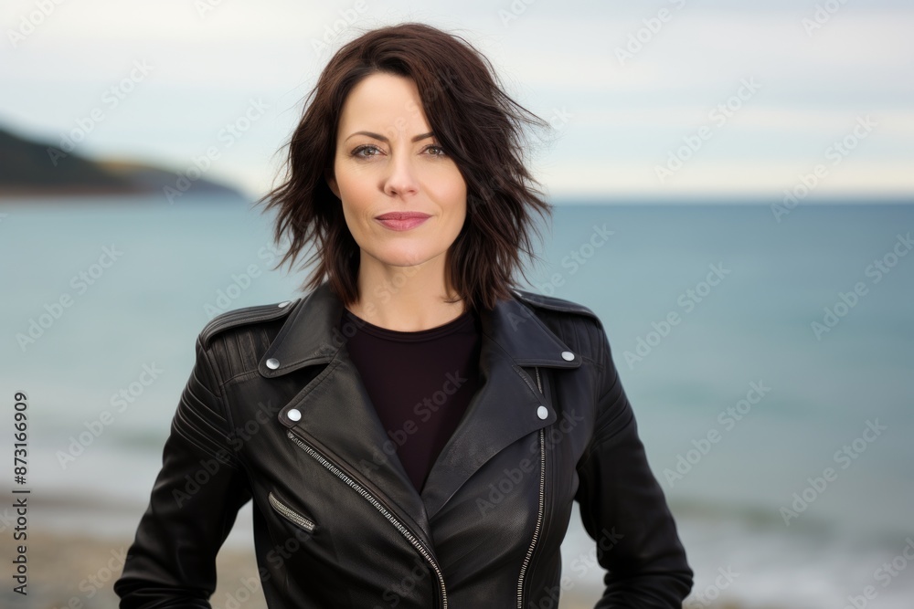 Portrait of a satisfied woman in her 40s sporting a classic leather jacket in serene seaside background Portrait of a satisfied woman in her 40s sporting a classic leather jacket in serene seaside background