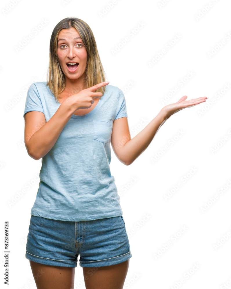 Young beautiful woman over isolated background amazed and smiling to the camera while presenting with hand and pointing with finger. Young beautiful woman over isolated background amazed and smiling to the camera while presenting with hand and pointing with finger.