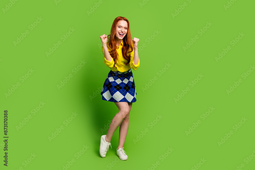 Photo portrait of lovely young lady raise fists winning celebrate dressed stylish yellow garment isolated on green color background Photo portrait of lovely young lady raise fists winning celebrate dressed stylish yellow garment isolated on green color background