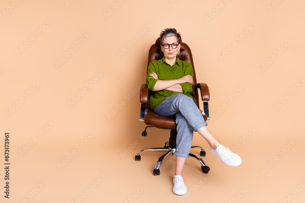 Full body photo of attractive retired woman sit armchair crossed hands dressed stylish green clothes isolated on beige color background Full body photo of attractive retired woman sit armchair crossed hands dressed stylish green clothes isolated on beige color background