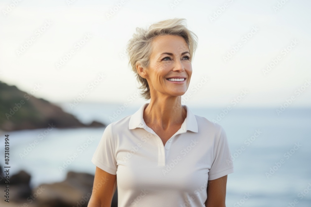 Portrait of a happy woman in her 50s wearing a sporty polo shirt while standing against calm bay background Portrait of a happy woman in her 50s wearing a sporty polo shirt while standing against calm bay background