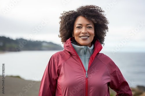 Portrait of a glad afro-american woman in her 50s wearing a functional windbreaker in calm bay background photo