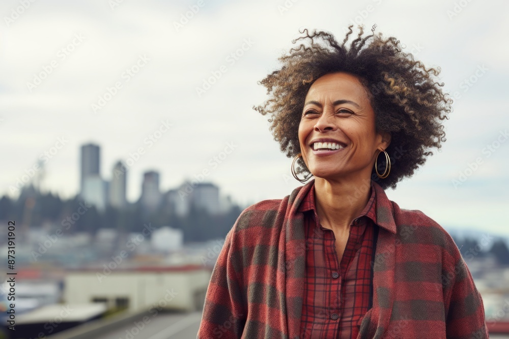 Portrait of a cheerful afro-american woman in her 50s wearing a comfy flannel shirt isolated in modern cityscape background Portrait of a cheerful afro-american woman in her 50s wearing a comfy flannel shirt isolated in modern cityscape background
