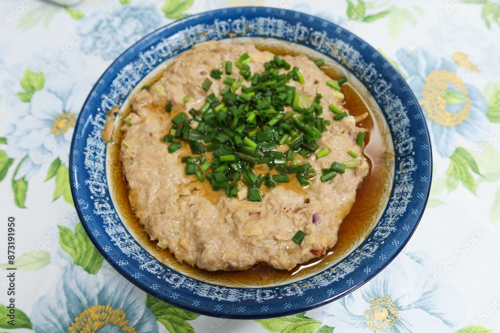close up top shot of Hong Kong Cantonese style homemade steamed pork meat patty with spring onion as toppings and soy sauce in a white and blue plate with white floral table cloth close up top shot of Hong Kong Cantonese style homemade steamed pork meat patty with spring onion as toppings and soy sauce in a white and blue plate with white floral table cloth