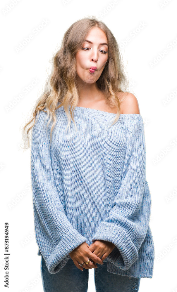 Beautiful young blonde woman wearing winter sweater over isolated background making fish face with lips, crazy and comical gesture. Funny expression.