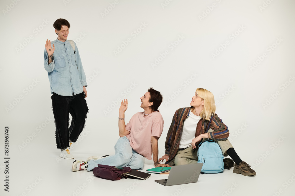 Fototapeta premium Three young students, dressed in casual attire, stand and sit on a white background, displaying camaraderie and connection.