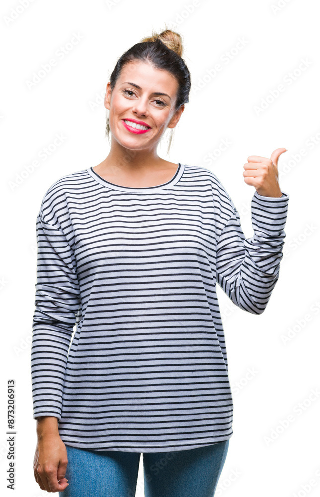 Young beautiful woman casual stripes sweater over isolated background smiling with happy face looking and pointing to the side with thumb up. Young beautiful woman casual stripes sweater over isolated background smiling with happy face looking and pointing to the side with thumb up.
