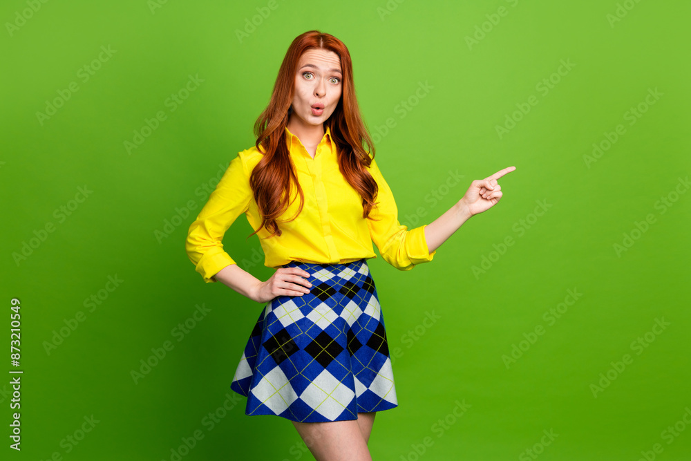 Photo portrait of lovely young lady point amazed empty space dressed stylish yellow garment isolated on green color background Photo portrait of lovely young lady point amazed empty space dressed stylish yellow garment isolated on green color background
