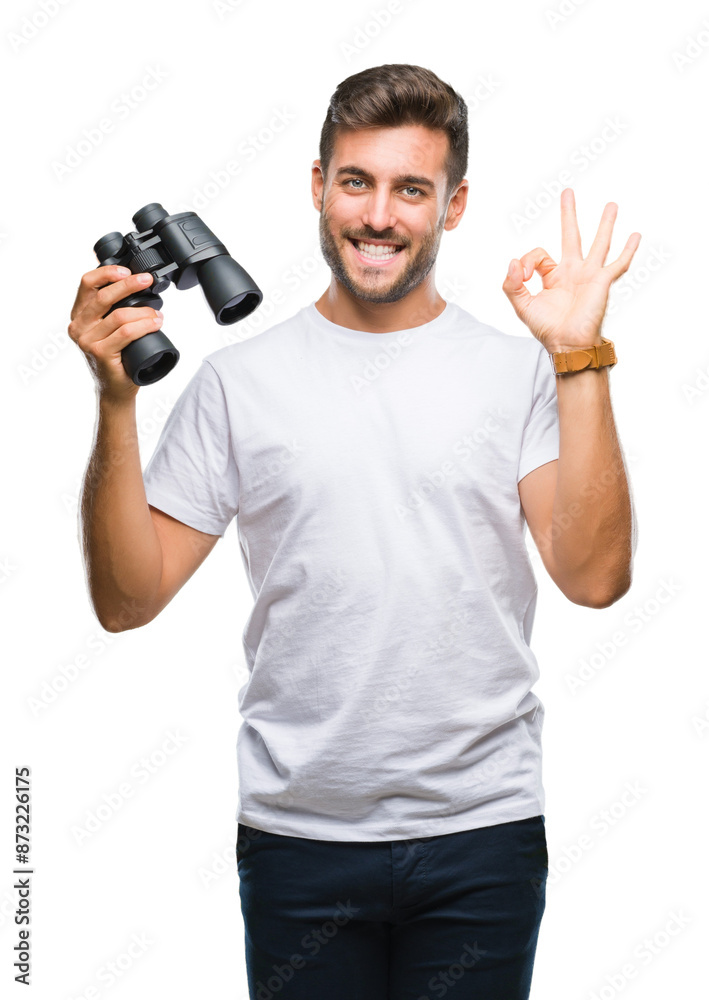 Young handsome man looking through binoculars over isolated background doing ok sign with fingers, excellent symbol Young handsome man looking through binoculars over isolated background doing ok sign with fingers, excellent symbol