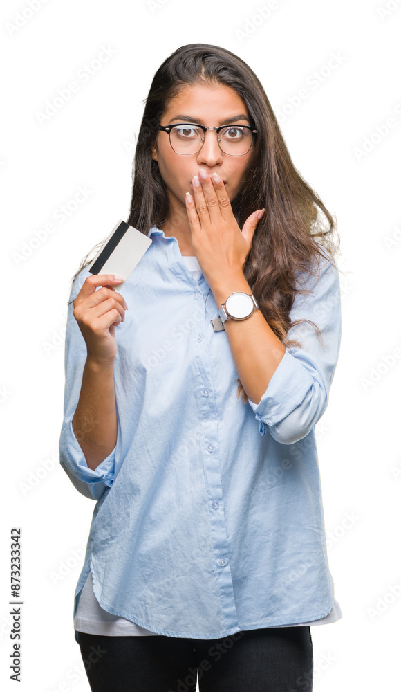 Young arab woman holding credit card over isolated background cover mouth with hand shocked with shame for mistake, expression of fear, scared in silence, secret concept Young arab woman holding credit card over isolated background cover mouth with hand shocked with shame for mistake, expression of fear, scared in silence, secret concept