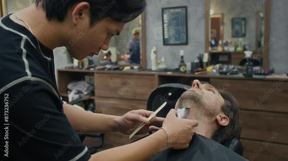 Medium shot of young Asian barber asking Caucasian client to raise his head while trimming his bristle at trendy salon Medium shot of young Asian barber asking Caucasian client to raise his head while trimming his bristle at trendy salon