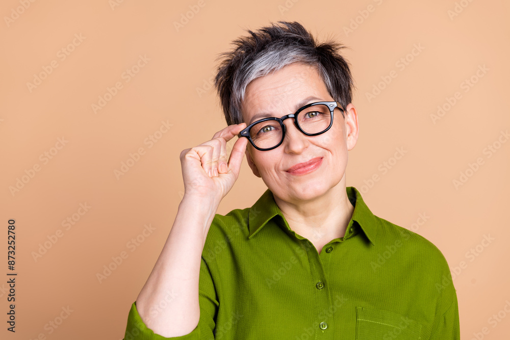 Photo portrait of attractive retired woman look camera touch specs dressed stylish green clothes isolated on beige color background