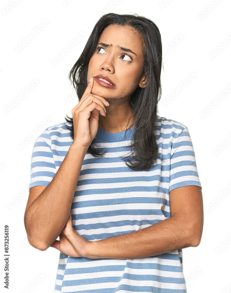 Young Latina posing in studio looking sideways with doubtful and skeptical expression.