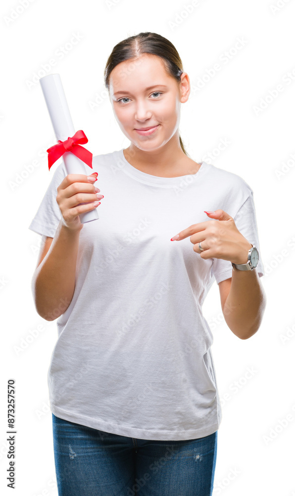 Young caucasian woman holding degree over isolated background with surprise face pointing finger to himself