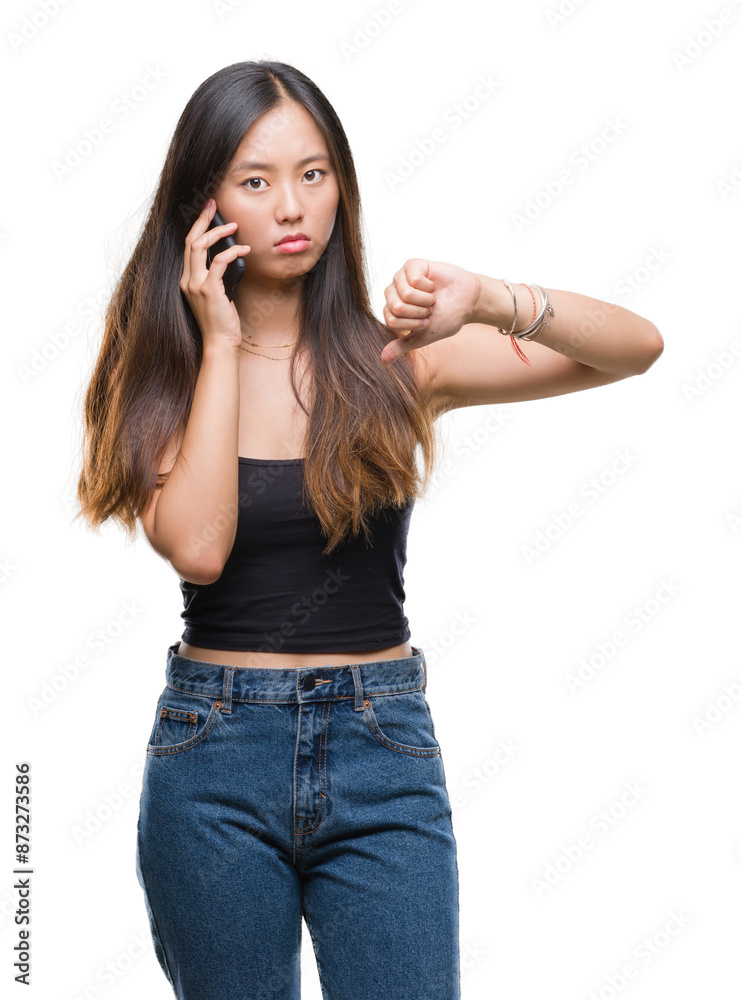 Young asian woman speaking on the phone over isolated background with angry face, negative sign showing dislike with thumbs down, rejection concept Young asian woman speaking on the phone over isolated background with angry face, negative sign showing dislike with thumbs down, rejection concept