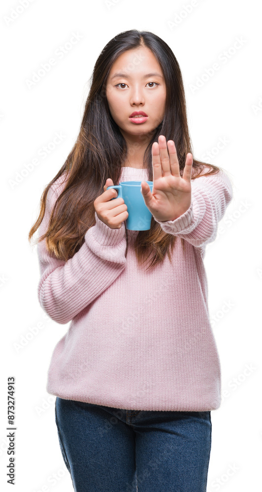 Young asian woman drinking coffee over isolated background with open hand doing stop sign with serious and confident expression, defense gesture Young asian woman drinking coffee over isolated background with open hand doing stop sign with serious and confident expression, defense gesture