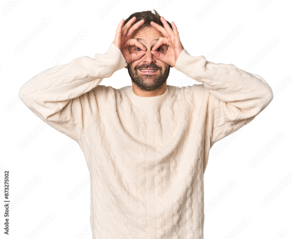 Studio portrait of young Hispanic male showing okay sign over eyes