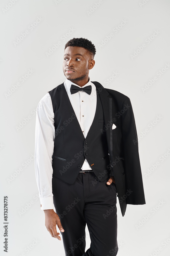 A young and handsome African American groom strikes a confident pose in a stylish tuxedo against a grey studio background. A young and handsome African American groom strikes a confident pose in a stylish tuxedo against a grey studio background.