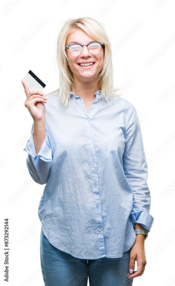 Young beautiful blonde business woman holding credit card over isolated background with a happy face standing and smiling with a confident smile showing teeth Young beautiful blonde business woman holding credit card over isolated background with a happy face standing and smiling with a confident smile showing teeth