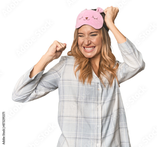 Blonde in pajamas with sleep mask celebrating a special day, jumps and raise arms with energy.