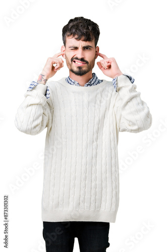 Young handsome man wearing winter sweater over isolated background covering ears with fingers with annoyed expression for the noise of loud music. Deaf concept.