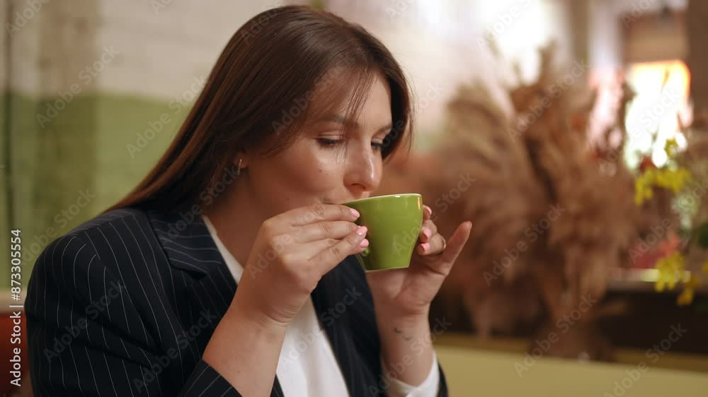 A woman holds a green cup of cappuccino with both hands and closes her eyes, inhaling the aroma of coffee. A woman drinks coffee from a porcelain cup while sitting at a table in a cafe A woman holds a green cup of cappuccino with both hands and closes her eyes, inhaling the aroma of coffee. A woman drinks coffee from a porcelain cup while sitting at a table in a cafe