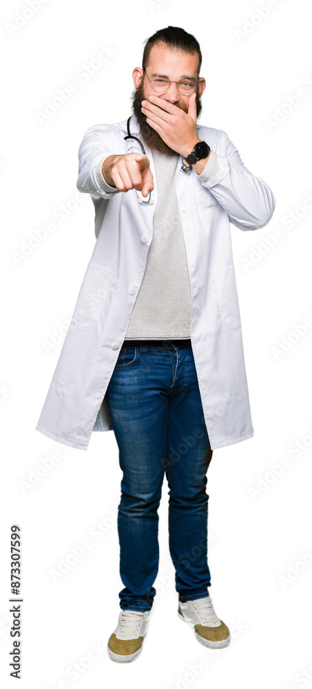 Young blond doctor man with beard wearing medical coat Laughing of you, pointing to the camera with finger hand over mouth, shame expression Young blond doctor man with beard wearing medical coat Laughing of you, pointing to the camera with finger hand over mouth, shame expression