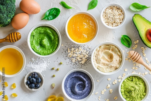 A flat lay of open containers filled with colorful natural face masks surrounded by fresh ingredients like honey, oats, avocado, and blueberries