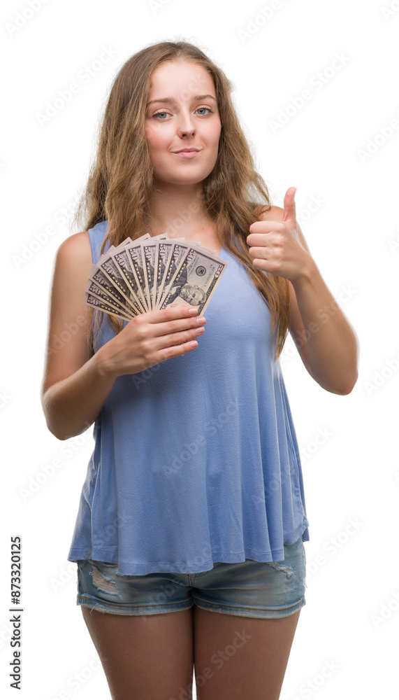 Young blonde woman holding dollars happy with big smile doing ok sign, thumb up with fingers, excellent sign Young blonde woman holding dollars happy with big smile doing ok sign, thumb up with fingers, excellent sign