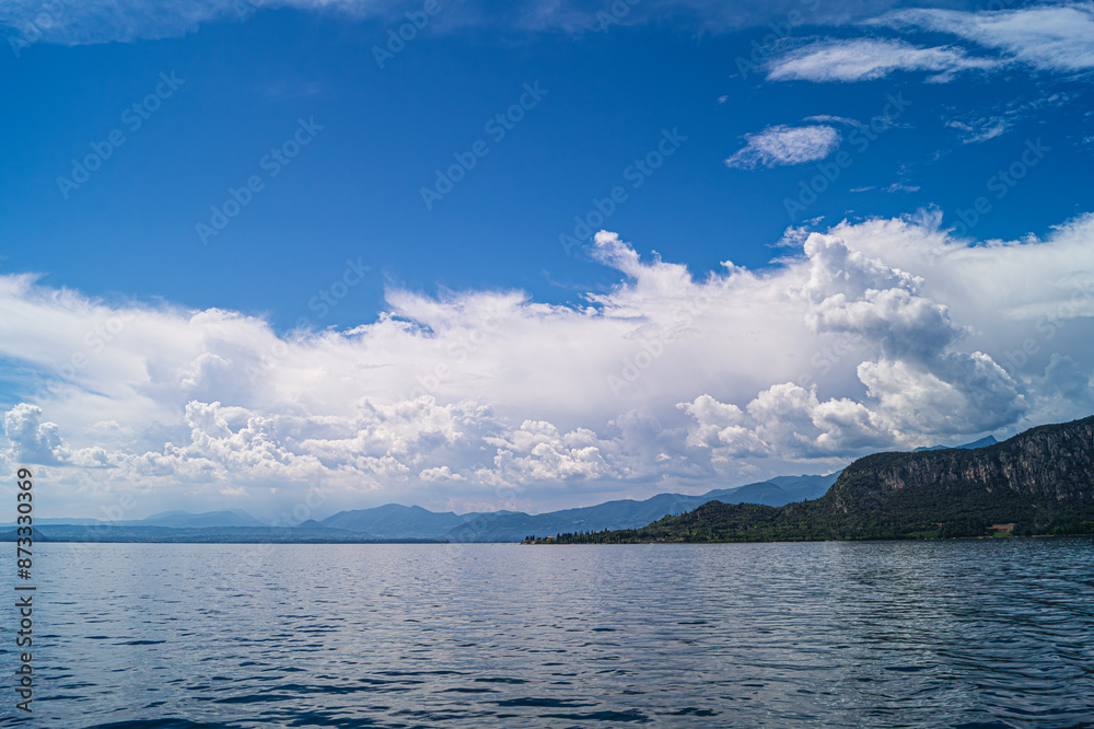A view of Lake Garda. Interesting cloud formations are reflected on the lake, with the surrounding hills and mountains on the horizon. A view of Lake Garda. Interesting cloud formations are reflected on the lake, with the surrounding hills and mountains on the horizon.