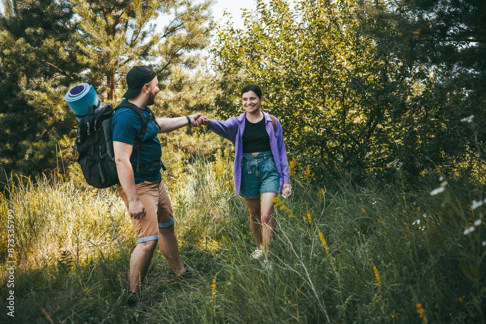 Fototapeta premium Happy couple tourists with backpacks walking outdoors in the summer forest