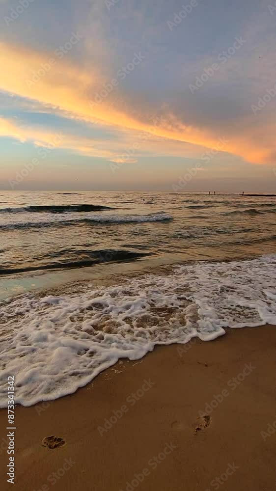 Dawn sunset sunrise on sea. The red light of dawn reflected by clouds in the blue sky and the surface of sea water. Waves rolling onto sandy beach of seashore. Vertical Dawn sunset sunrise on sea. The red light of dawn reflected by clouds in the blue sky and the surface of sea water. Waves rolling onto sandy beach of seashore. Vertical