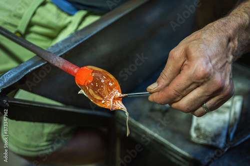 Close-up image of a glassblower forming hot molten glass under intense fire in a workshop, blast furnace. Manual processing of glass by masters inside the glass. Selective focus photo