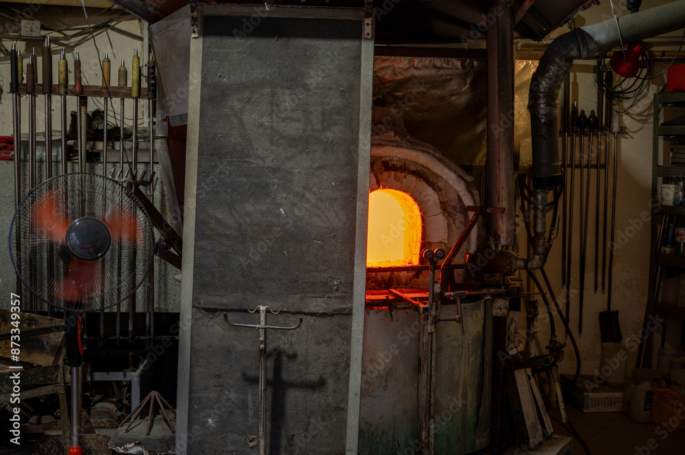 Close-up image of a glassblower forming hot molten glass under intense fire in a workshop, blast furnace. Manual processing of glass by masters inside the glass. Selective focus