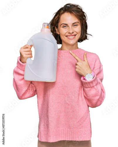 Young hispanic woman doing laundry holding detergent bottle smiling happy pointing with hand and finger