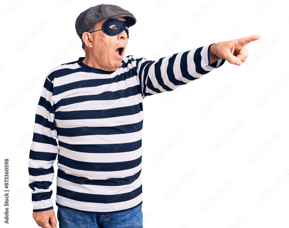 Senior handsome man wearing burglar mask and t-shirt pointing with finger surprised ahead, open mouth amazed expression, something on the front Senior handsome man wearing burglar mask and t-shirt pointing with finger surprised ahead, open mouth amazed expression, something on the front
