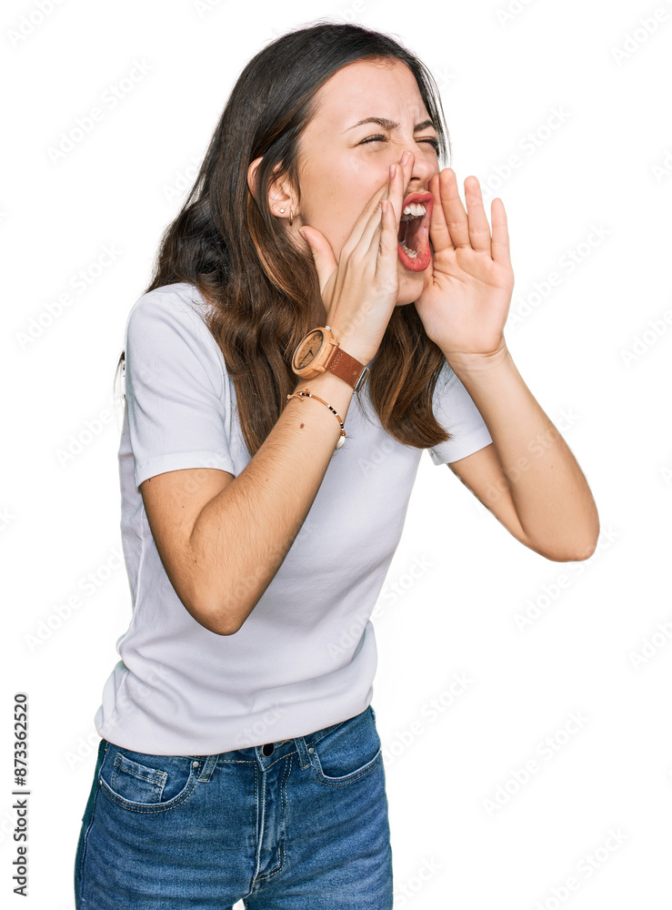Young beautiful woman wearing casual white t shirt shouting angry out loud with hands over mouth
