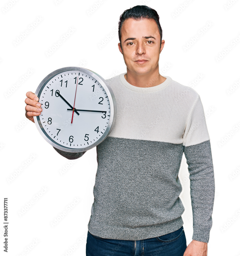 Handsome young man holding big clock thinking attitude and sober expression looking self confident Handsome young man holding big clock thinking attitude and sober expression looking self confident