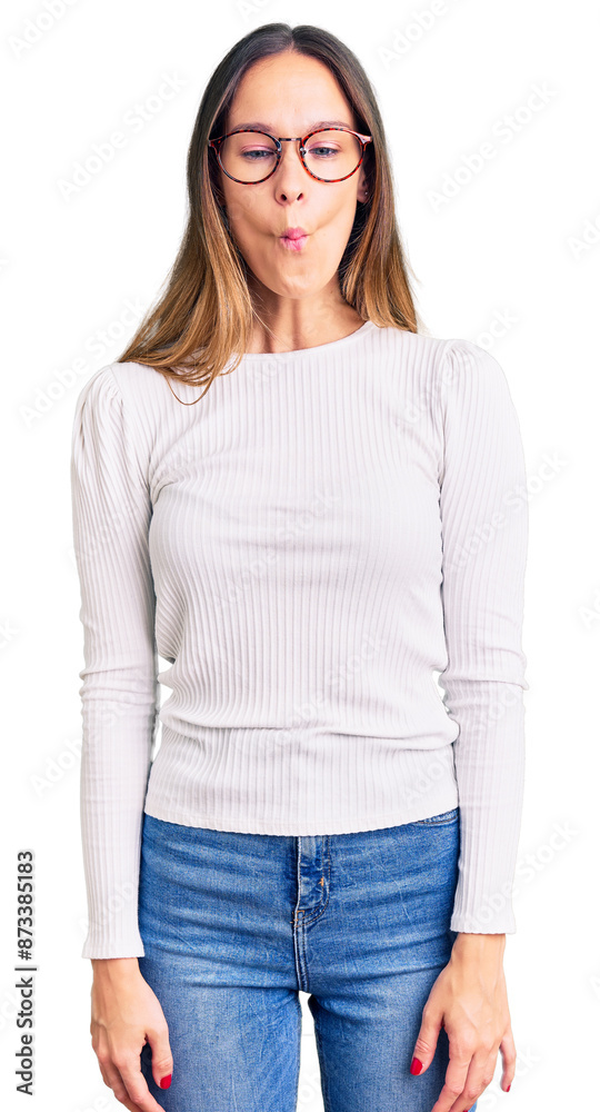 Beautiful brunette young woman wearing casual white sweater and glasses making fish face with lips, crazy and comical gesture. funny expression.
