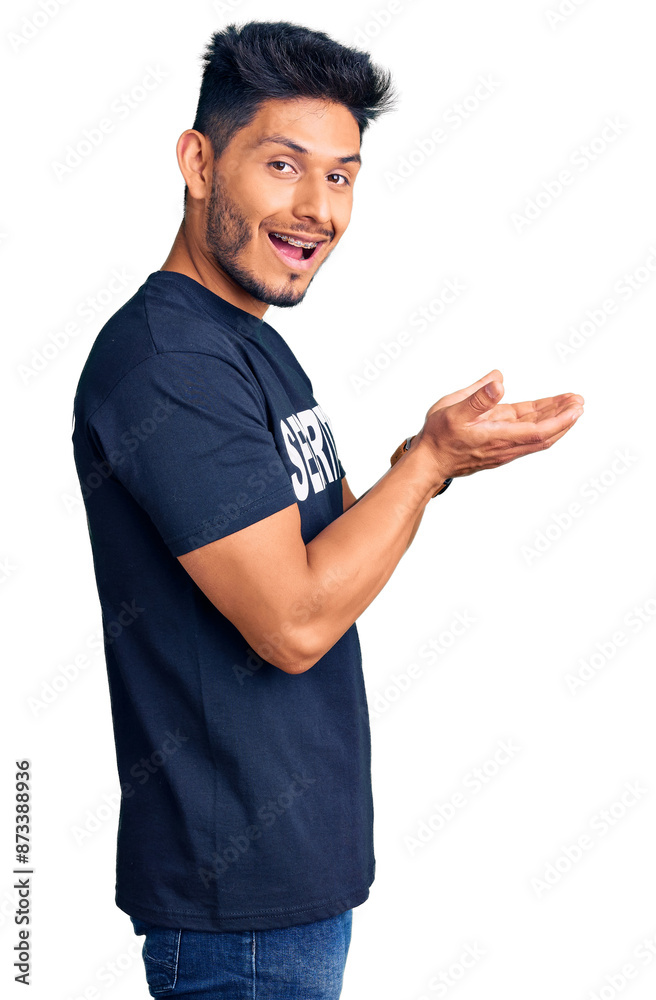 Handsome latin american young man wearing security t shirt pointing aside with hands open palms showing copy space, presenting advertisement smiling excited happy Handsome latin american young man wearing security t shirt pointing aside with hands open palms showing copy space, presenting advertisement smiling excited happy