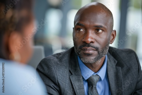 A serious man in a business suit attentively listens during a conversation, projecting focus and professionalism in a work or formal meeting setting.