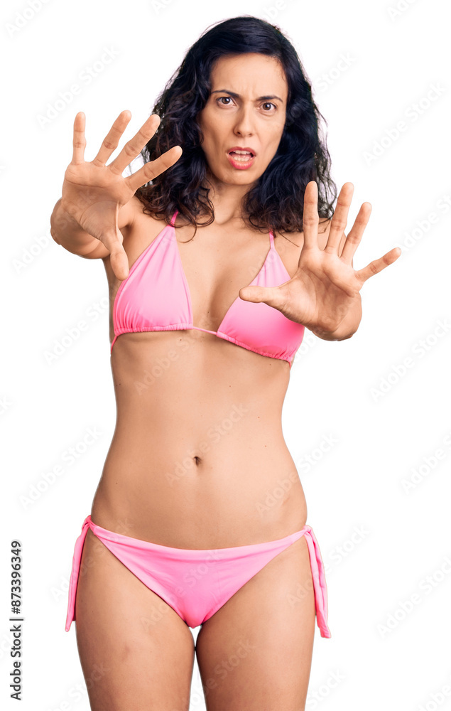Young beautiful hispanic woman wearing bikini doing stop gesture with hands palms, angry and frustration expression